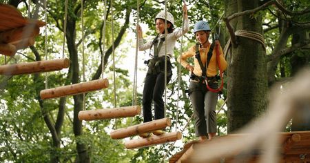Zwei Personen mit Helmen und Kletterausrüstung überqueren eine schwebende Holzbrücke im Kletterpark.