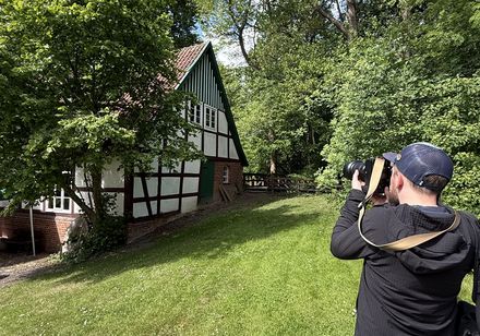 Mann fotografiert Fachwerkhaus in grüner Umgebung