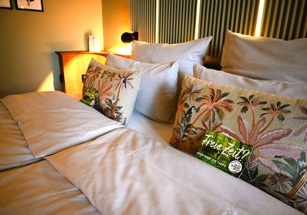 Bett im Hotelzimmer, vor den Kissen eine Karte zum Teuto-Navigator