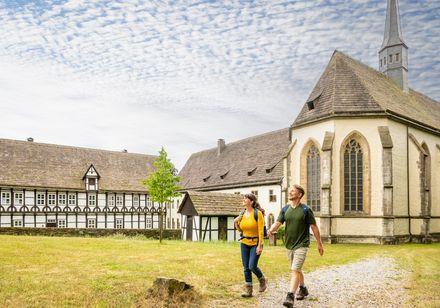 Zwei Wanderer vor Kloster Falkenhagen in Lügde mit Fachwerkgebäuden unter blauem Himmel.