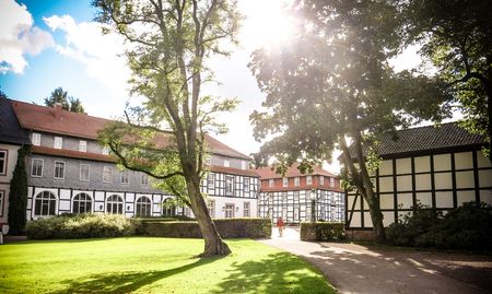 Historische Fachwerkgebäude und üppige Bäume in einem gepflegten Park bei Sonnenschein.