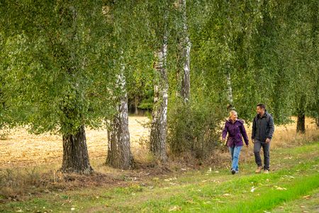 Zwei Personen spazieren über Feldweg, links von ihnen Bäume
