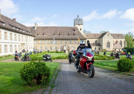 Motorradfahrer grüßen vor dem historischen Hotel Schloss Gehrden inmitten von gepflegten Grünanlagen.