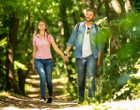 Paar beim Spaziergang auf einem sonnigen Waldweg, umgeben von üppigem, grünem Laub.
