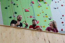 Personen lehnen über Holzwand, im Hintergrund eine Kletterwand