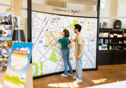 Eine Frau und ein Mann betrachten eine große, detaillierte Stadtkarte in einem Besucherzentrum.