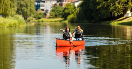 Zwei Personen paddeln im roten Kanu auf einem ruhigen Fluss, umgeben von grüner Natur.