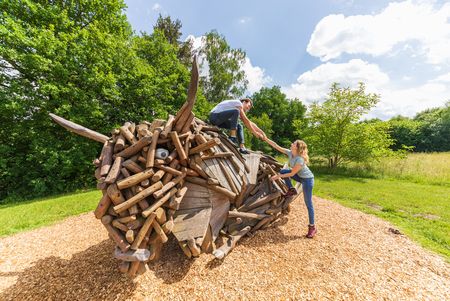Zwei Personen klettern auf Wisentfigur aus Holz