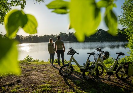 Zwei Personen neben Fahrrädern schauen Sonnenuntergang beim Verler See an