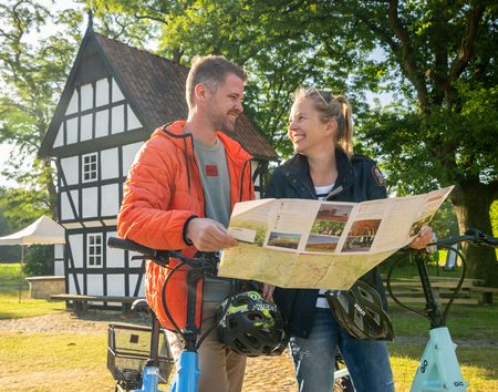Zwei Personen stehen neben ihren Fahrrädern, schauen sich an und halten eine Karte