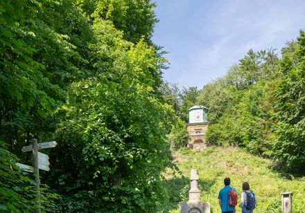 Zwei Wanderer in grüner Natur schauen Denkmal an