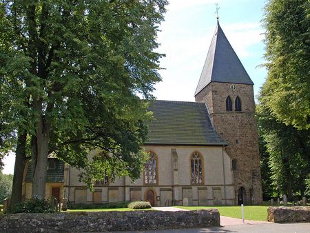 Stiftskirche in Stift Quernheim mit steinernem Glockenturm und umgebenden Laubbäumen im Sommer.
