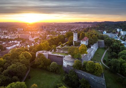 <p>Luftaufnahme der Sparrenburg in Bielefeld im goldenen Licht der untergehenden Sonne.</p>