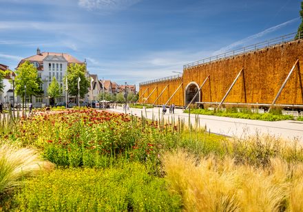 Gradierwerk mit Solewand in einer Parkanlage, umgeben von blühenden Pflanzen und einem klaren Himmel.