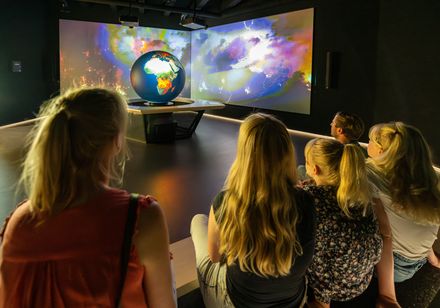 Familie sitzt in der Klimaerlebniswelt Oerlinghausen und schaut beleuchteten Globus und Film an