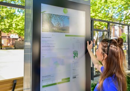 Eine Frau bedient eine digitale Stele im Teutoburger Wald in Herzebrock-Clarholz bei Sonnenschein.