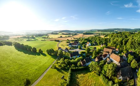 Weite Landschaft in Detmold, grüne Felder, Wald und verstreute Höfe unter klarem, blauem Himmel.