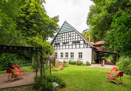 Fachwerkhaus im Grünen mit Liegestühlen, umgeben von üppiger Vegetation und entspannter Gartenatmosphäre.