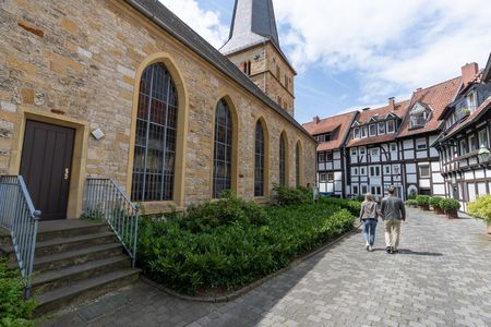 Älteres Paar spaziert an einer historischen Kirche mit Fachwerkhäusern im Hintergrund entlang.