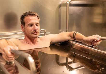 Mann entspannt mit geschlossenen Augen in einer metallenen Wanne mit dunklem Moorbad.