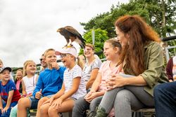 Eine Gruppe von Kindern und Erwachsenen beobachtet fasziniert einen Greifvogel, der auf dem Kopf eines Mädchens sitzt.