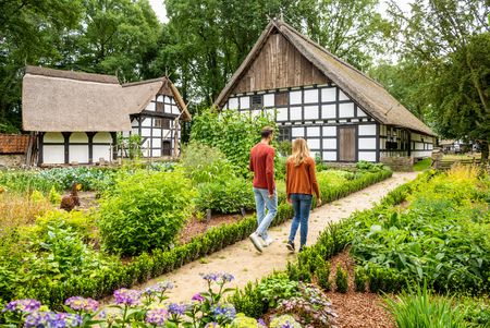 Ein Paar spaziert durch Garten im Museumshof Rahden mit historischen Fachwerkhäusern im Hintergrund in Rahden.