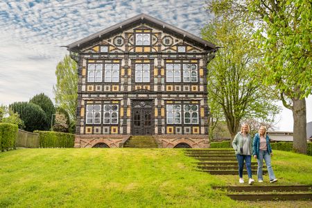 Historisches Fachwerkhaus mit aufwendiger Fassade, zwei Frauen stehen davor auf einer Treppe.