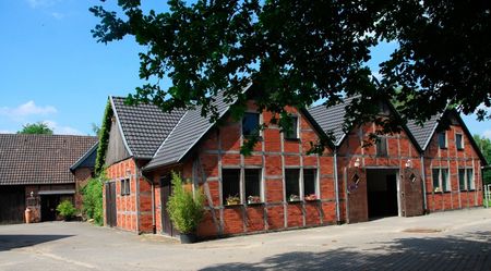Außenansicht eines traditionellen Backsteinhauses mit Satteldach unter blauem Himmel, umgeben von Bäumen.