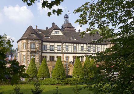Schloss Heerse präsentiert sich mit Fachwerkarchitektur, umgeben von gepflegtem Garten und Bäumen.