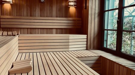Holzverkleidete Sauna mit großen Bänken, warmem Licht und einem Fenster mit Blick nach draußen.