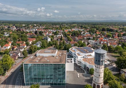 Luftaufnahme einer modernen Bibliothek mit gläserner Fassade und historischem Wasserturm im Stadtzentrum.