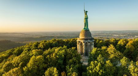 Hermann-Denkmal im Teutoburger Wald bei Sonnenuntergang, umgeben von dicht bewaldeten Hügeln.