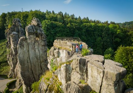 Zwei Personen genießen die Aussicht von einer Plattform auf den beeindruckenden Externsteinen.