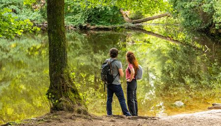 Zwei Wanderer stehen am Ufer eines idyllischen Waldbachs, umgeben von üppigem Grün der Natur.