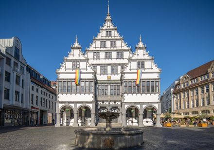 Renaissance-Rathaus mit prächtiger Fassade und Schaugiebeln, im Vordergrund ein runder Brunnen.