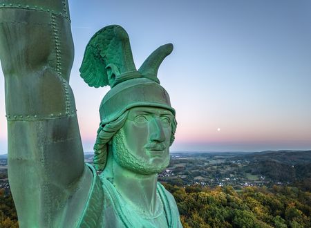 Hermann-Denkmal im Teutoburger Wald bei Sonnenuntergang, mit Ausblick über bewaldete Hügel und Dörfer.