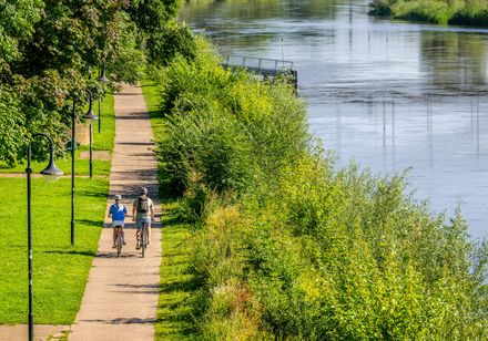 Zwei Radfahrer fahren neben der Weser auf einem Weg im Grünen
