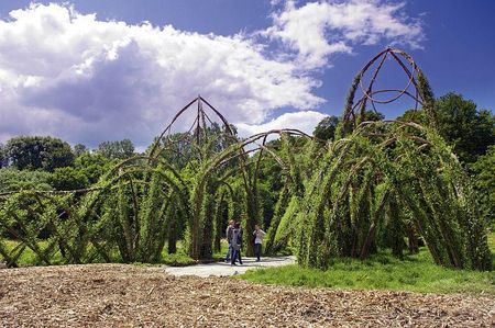 Ein kunstvoll geformtes Weidengeflecht mit Menschen auf einem Pfad, umgeben von üppigem Grün.