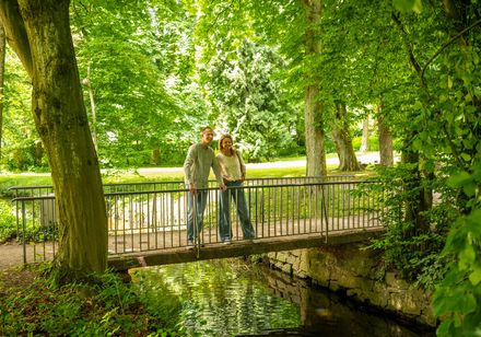 Zwei Personen stehen auf einer kleinen Brücke in grüner Natur des Kurparks Bad Meinberg