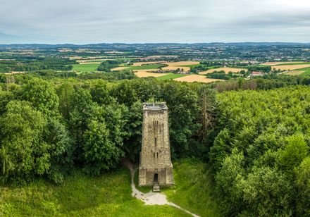 <p>Alter Aussichtsturm umgeben von dichten Wäldern und Hügeln unter einem weiten, bewölkten Himmel.</p>