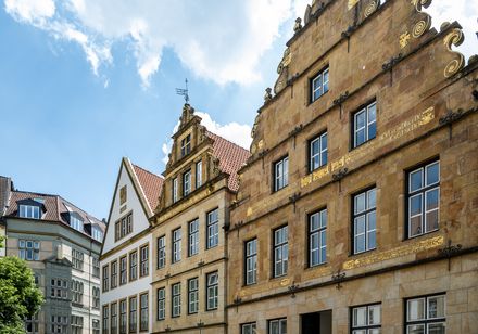 Historische Häuserfassaden in Osnabrück unter blauem Himmel mit Wolken und dekorativen Giebeln.