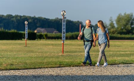 Ein Paar spaziert Hand in Hand über einen Kiesweg in einer grünen Parklandschaft.