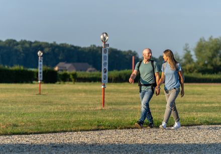 Ein Paar spaziert Hand in Hand über einen Kiesweg in einer grünen Parklandschaft.