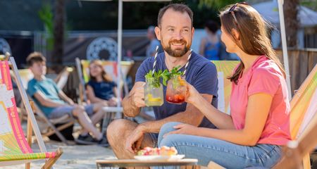 Ein Paar entspannt in Liegestühlen bei Sonnenschein und genießt erfrischende Getränke am Strand.