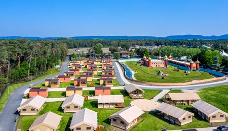 Luftaufnahme eines weitläufigen Erlebnisresorts mit Zelten, Grünflächen und einer Wasseranlage im Zentrum.