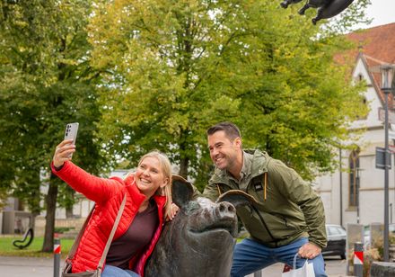 Zwei Personen hocken um eine Schweinefigur - Wurstträgerbrunnen Versmold