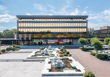Das Bild zeigt die moderne Fassade des Heinz Nixdorf MuseumsForums in Paderborn vor blauem Himmel.