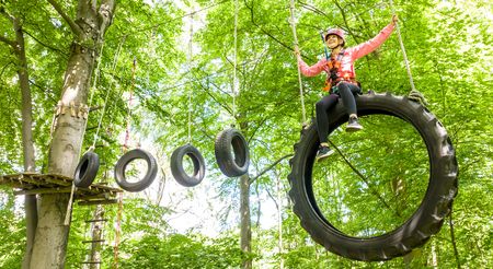 <p>Kind klettert im Park auf Baumhindernis mit Reifen, umgeben von grünen Blättern.</p>