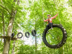 <p>Kind klettert im Park auf Baumhindernis mit Reifen, umgeben von grünen Blättern.</p>