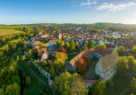 Luftaufnahme von Blomberg im Sonnenlicht, mit historischen Gebäuden, grünen Hügeln und Windrädern.